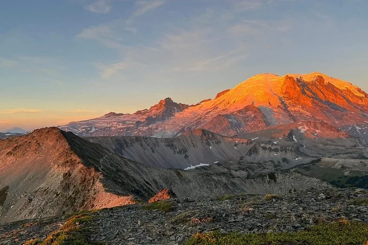 La luz del sol ilumina la cima del Monte Rainier sobre un paisaje alpino escarpado.